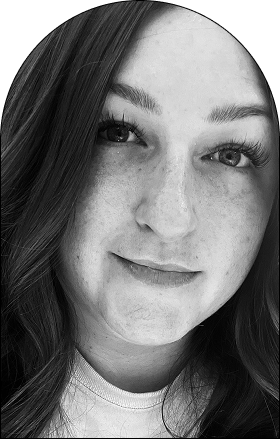 Black and white close-up portrait of a woman with long wavy hair, light skin, and visible freckles, looking directly at the camera with a slight smile. The rounded top adds a modern design concept to this striking salon-inspired image.