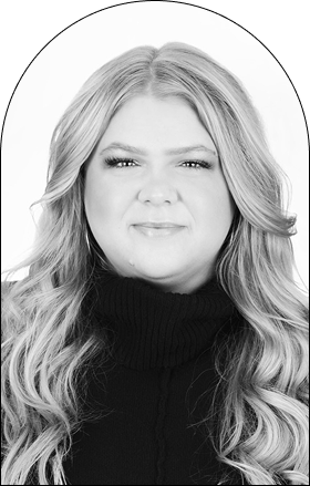 Black and white portrait of a woman with long, wavy hair wearing a dark turtleneck sweater, looking directly at the camera with a neutral expression—a refined style echoing leading Salon design concepts in Corpus Christi.