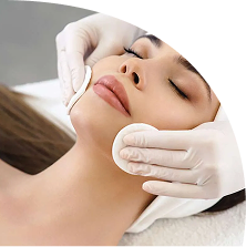 A person with closed eyes enjoys a relaxing spa facial treatment; someone in white gloves, typical of a salon or spa, gently applies cotton pads to their face.