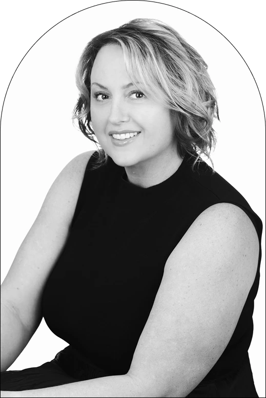 A woman with wavy, shoulder-length hair and a sleeveless black top smiles at the camera in a black-and-white portrait with a white background and oval frame, capturing elegant design concepts inspired by Corpus Christi style.
