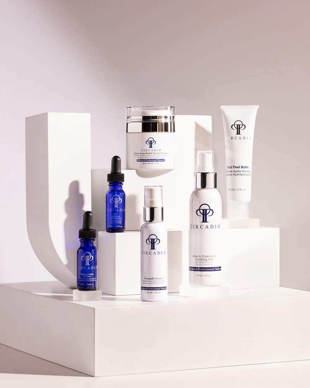 A collection of Circadia Skincare products, including bottles, jars, and tubes, are arranged on white geometric platforms with a softly lit background. The sleek white and blue packaging features the Circadia logo prominently.